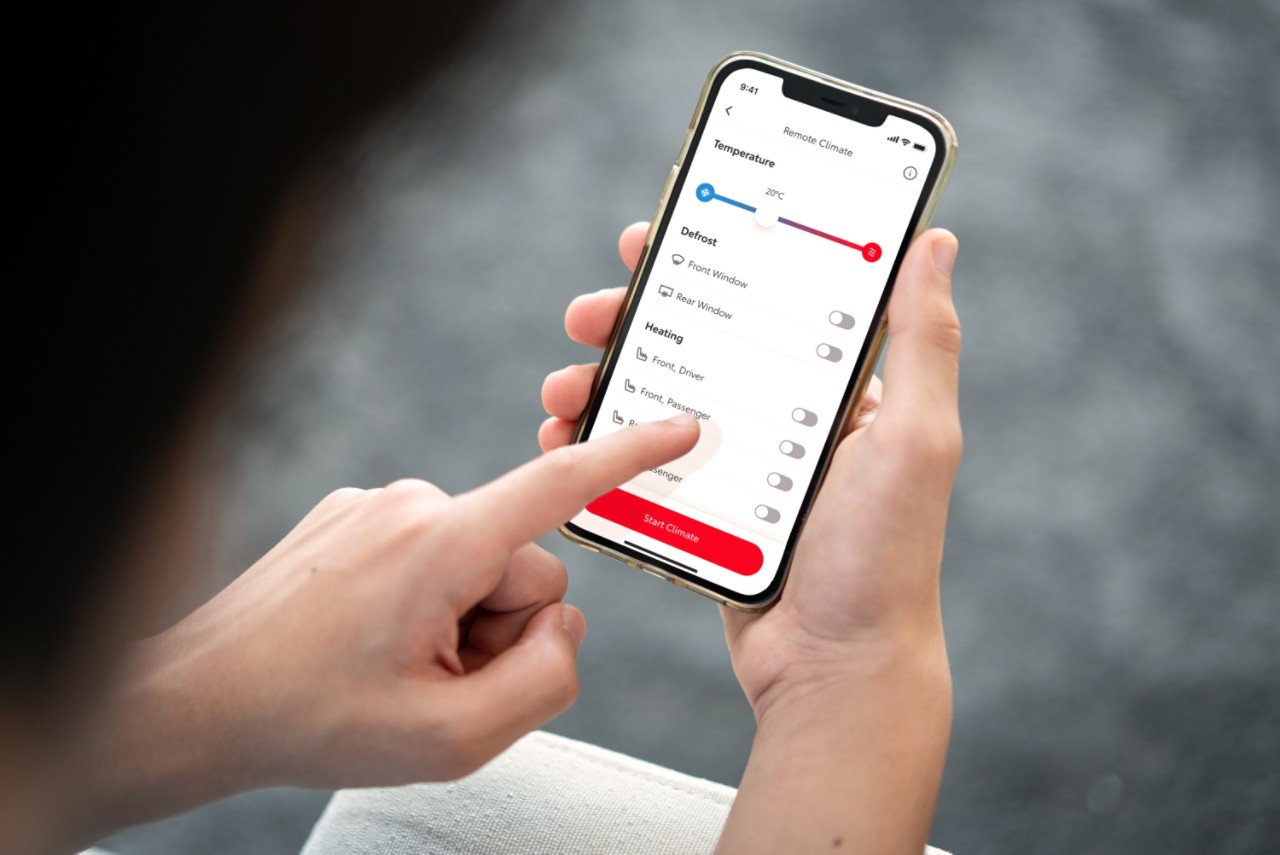 Žmogus laiko išmanųjį telefoną, kuriame rodoma programėlė MyToyota. Kairiąja ranka jis baksteli ekraną, kad nuotoliniu būdu nustatytų savo automobilio klimato kontrolę.